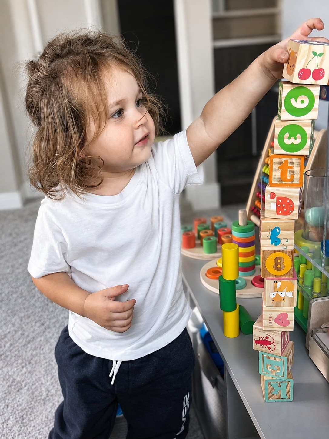 A child reaching to stack an alphabet block tower