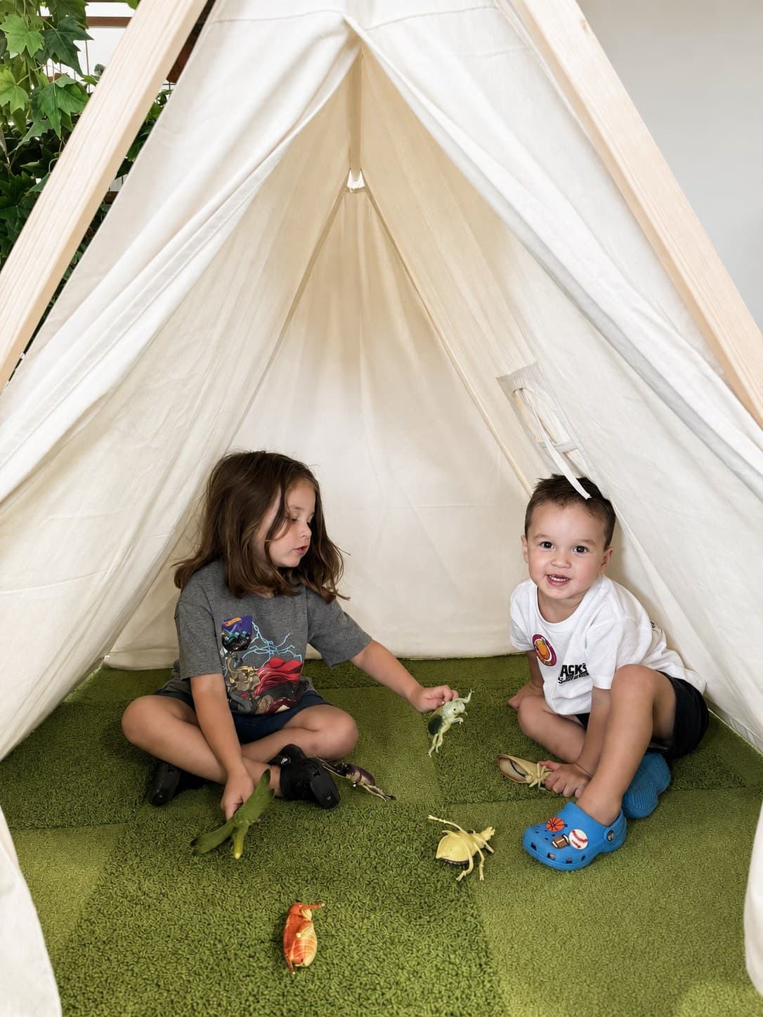 Two children playing with toy animals inside a canvas teepee