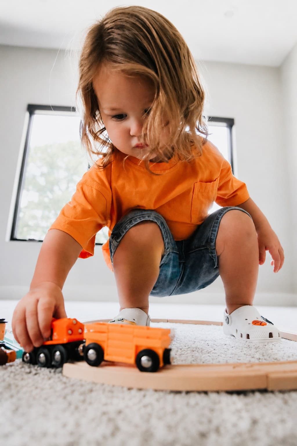 A toddler playing with a wooden train set on the floor
